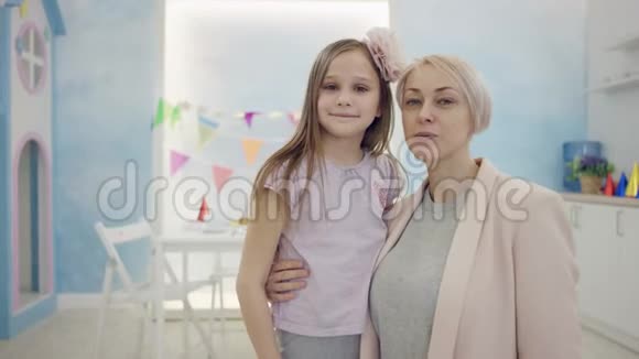 成年女性和小女孩在房间里的镜头前拥抱并展示拇指手指视频的预览图