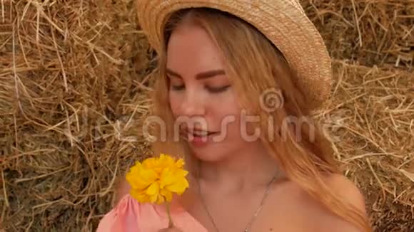 一个年轻迷人的女孩戴着草帽心情愉快地嗅着一朵黄色的花然后从他身上流下花瓣把它们从她的爸爸身上吹下来视频的预览图
