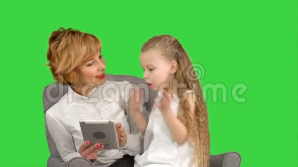 年轻的母亲和女儿坐在一起看着绿色屏幕上的平板电脑Chroma键视频的预览图