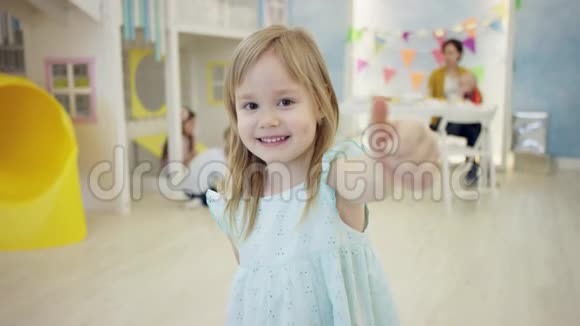 可爱的小女孩正在镜头前竖起大拇指而其他孩子则在房间里的背景上玩耍视频的预览图
