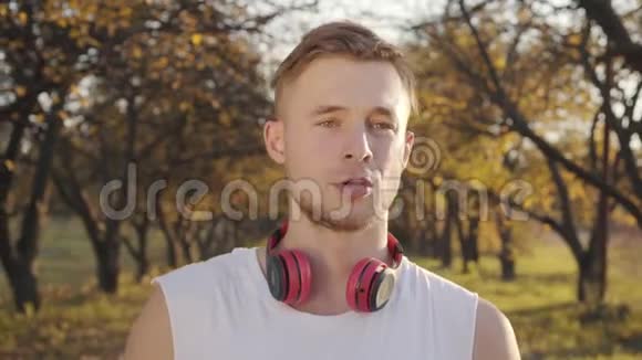 白种人年轻运动男孩站在秋天公园和饮用水的肖像英俊的运动员视频的预览图