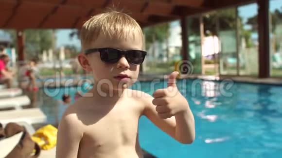 泳池背景上戴太阳镜的微笑小男孩的肖像慢动作视频的预览图