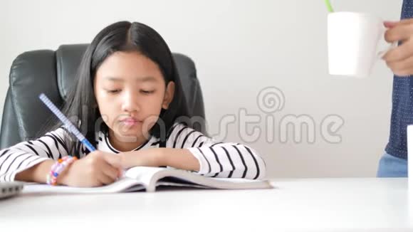 母亲给女儿一个白色的杯子亚洲小女孩在做家庭作业时快乐地自学和家庭教育视频的预览图