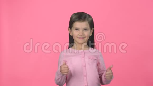 布鲁内特的孩子微笑着在粉红色的背景上竖起大拇指视频的预览图