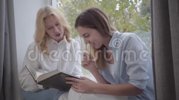 年轻漂亮的白种人女人和年长的金发女人在看照片母女在家分享回忆快乐视频的预览图