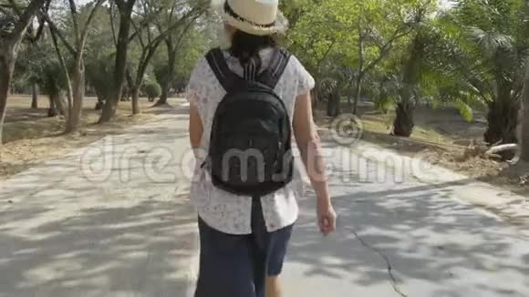 带背包戴草帽的亚洲女人的后景在公共公园的马路上行走视频的预览图