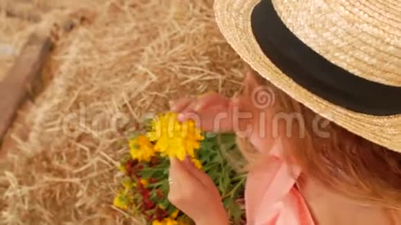 一个年轻漂亮的女孩戴着草帽坐在干草上手里拿着一朵黄色的花然后闻了闻4k4k视频视频的预览图