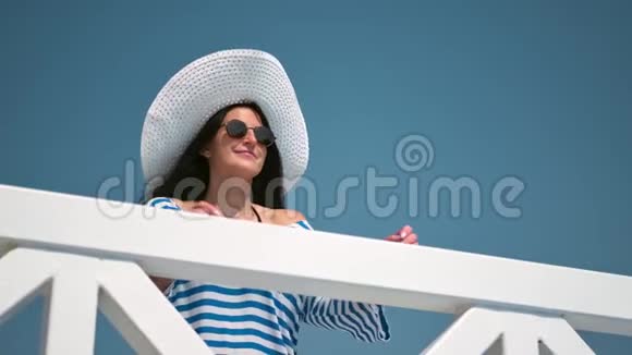 带着时髦墨镜和白帽子的微笑放松的女人享受阳台中档的假期视频的预览图