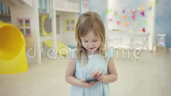 一个迷人的小女孩正在房间里镜头前的智能手机屏幕上滑动视频的预览图