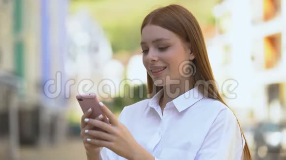 在户外智能手机上发出快乐的白种人女孩信息微笑应用程序视频的预览图