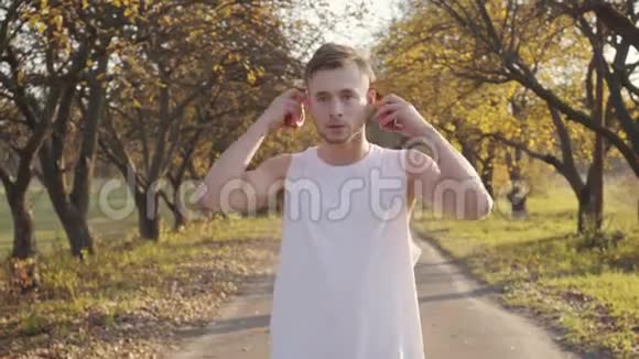 穿着运动服的年轻白种人男孩戴上耳机开始在秋季公园跳绳锻炼田径视频的预览图