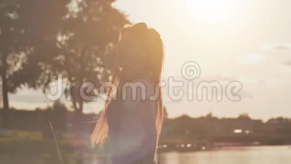 长头发的金发女孩正在湖边柔和的日落背景下旋转视频的预览图