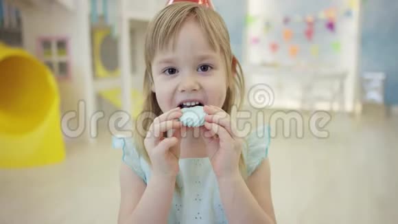 漂亮的小女孩在游戏室里在镜头前戴着锥帽吃棉花糖视频的预览图