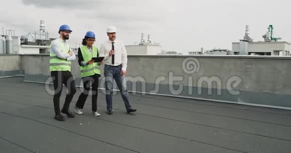 在现代建筑工地的屋顶上一位商人一个成熟的人和两个工程师分析了视频的预览图