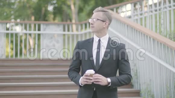 肖像年轻雄心勃勃的成功商人站在公园楼梯上喝咖啡办公室经理视频的预览图