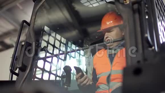 操作人员戴着头盔穿着工作服坐在新的装载机和操作车上接电话视频的预览图
