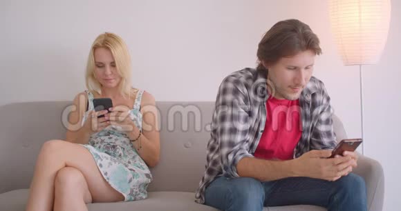 一对有魅力的白种人夫妇使用电话和分享滑稽的帖子坐在沙发上的特写照片视频的预览图