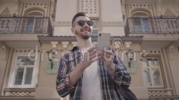 留着胡子的年轻人穿着格子衬衫和太阳镜在研究城市的建筑时环顾四周一位游客视频的预览图