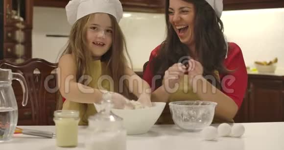 开朗的白种人母女在厨房一起做饭小女孩拍手面粉飞扬视频的预览图