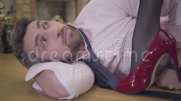 一个英俊的白发白人男子躺在地板上的特写脸穿红色高跟鞋的漂亮女腿视频的预览图