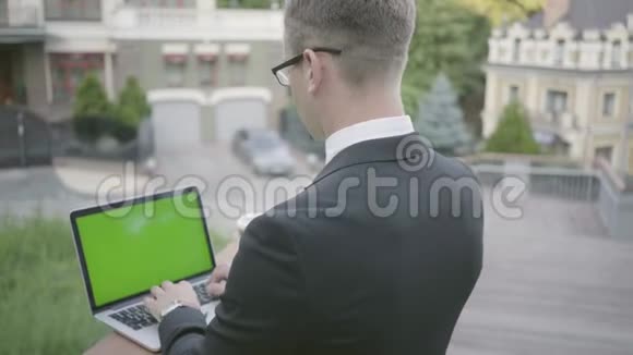 年轻雄心勃勃衣着考究的商人站在露台上用绿色屏幕制作上网本视频的预览图