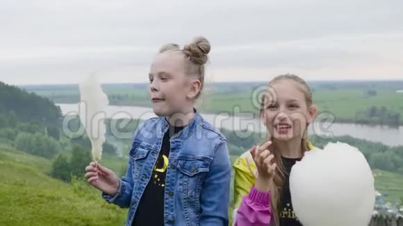 两个十几岁的女孩在夏天的森林和河流景观上吃甜棉花带着甜美棉花的女朋友视频的预览图