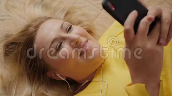 一个美丽的女人躺在床上一边用智能手机听音乐视频的预览图