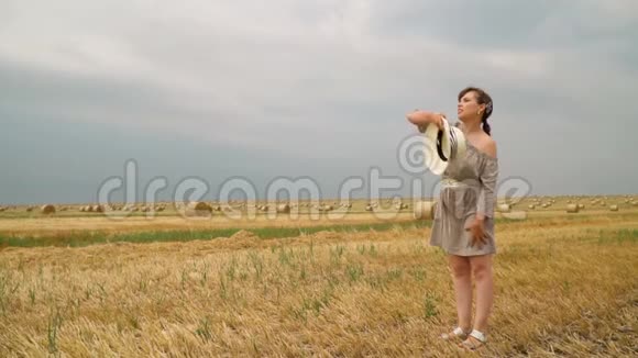 在夏天的傍晚年轻女子把帽子扔在一片麦田的地上视频的预览图