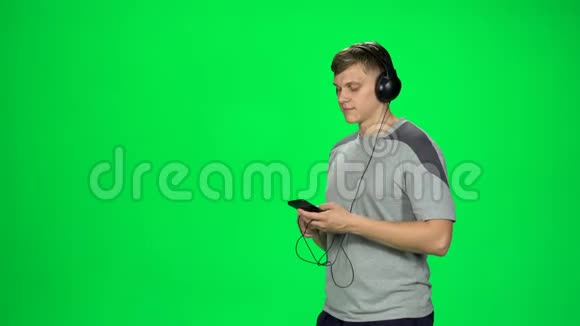 男的戴着黑色大耳机在工作室的绿色屏幕上用智能手机发短信视频的预览图