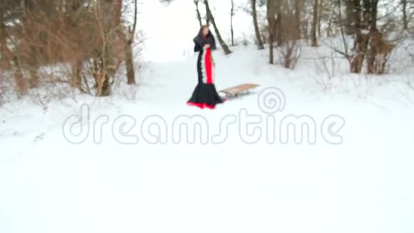 一个披着羽绒披肩的漂亮女孩在雪地里背着雪橇迎着冬日的森林视频的预览图