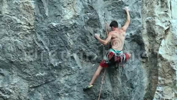 后景年轻的肌肉男攀岩者在垂直悬崖的户外艰难运动路线上攀爬视频的预览图