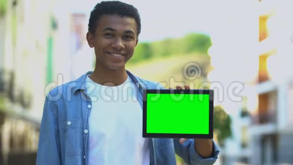 兴奋的黑人男孩手指着手中的绿色屏幕平板电脑做广告视频的预览图