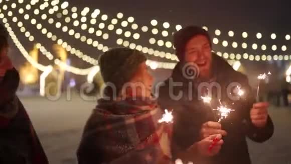 一群朋友玩着手里拿着火花挥舞快乐的人们在冬天的夜晚与降雪狂欢视频的预览图