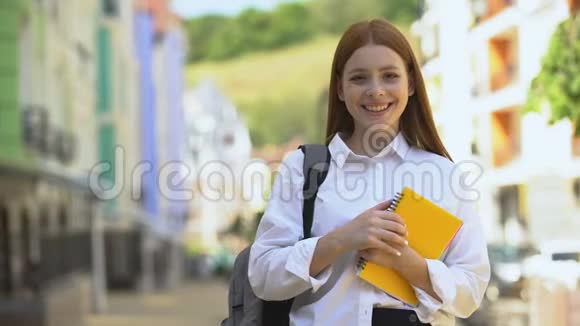 快乐的女高中学生带着背包和书竖起大拇指视频的预览图