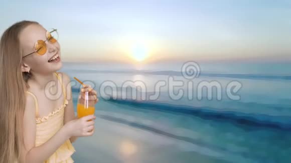 笑的女孩手里拿着橙汁杯在海上日落的背景下戴黄色眼镜的快乐少女视频的预览图