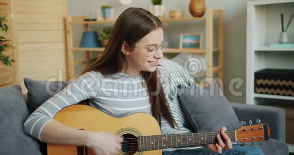 戴眼镜的年轻女士在家弹吉他享受音乐和闲暇时光视频的预览图