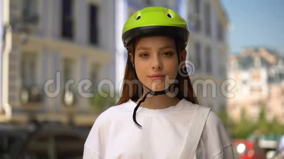 戴着防护头盔的快乐少女在相机上微笑骑自行车积极爱好视频的预览图