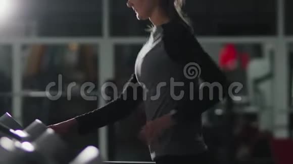 漂亮的棕色头发的女人在健身房黑暗的房间里的跑步机上从事体育锻炼视频的预览图