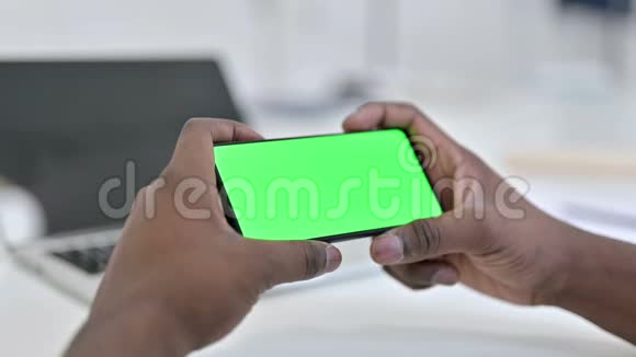 非洲男子手在绿色智能手机屏幕上观看视频视频的预览图