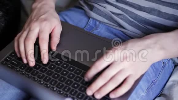 一个白种人坐在宠物狗旁边的床上手拿笔记本电脑打字视频的预览图