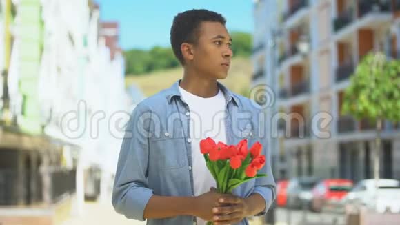 紧张的年轻男性带着郁金香花束在街上等待女孩第一次约会视频的预览图