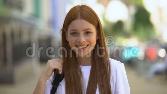 年轻漂亮的女性带着背包在相机上微笑抚摸头发调情视频的预览图