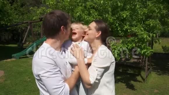 可爱的父母拥抱和亲吻可爱的男孩在夏天的花园手持射击视频的预览图