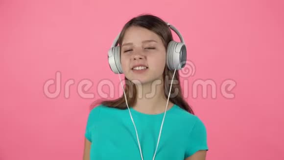 青少年女性听音乐和舞蹈在粉红色背景的白色大耳机慢动作视频的预览图