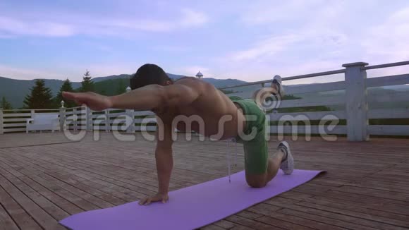 年轻的壮汉在户外的紫罗兰瑜伽垫上伸展视频的预览图