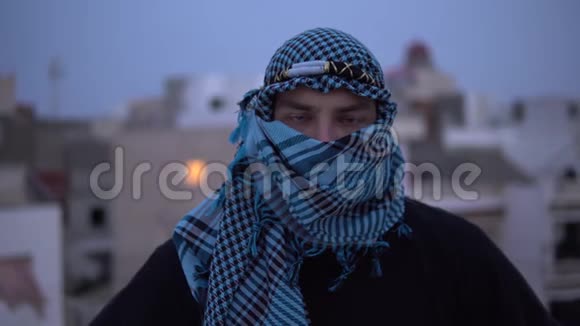 戴阿拉伯手帕的年轻人一个人看着相机打开手帕在房子的屋顶上视频的预览图
