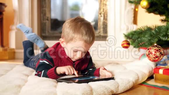 4k小男孩的特写视频数字平板电脑躺在圣诞树和壁炉旁边的客厅地板上视频的预览图