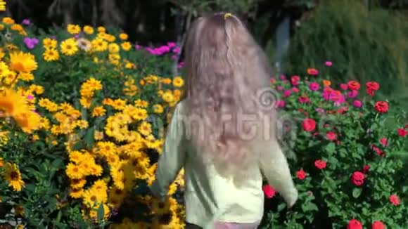 可爱的女孩金色的卷发抚摸着夏天盛开的五颜六色的花朵视频的预览图