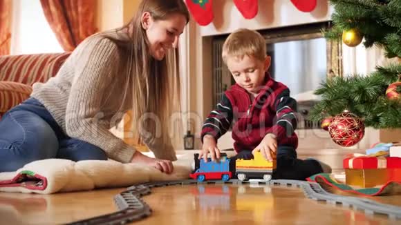 小蹒跚学步的男孩在圣诞树下的地板上玩耍时把玩具车连接到火车上的4k镜头儿童视频的预览图
