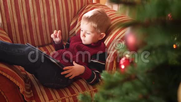 圣诞节后早晨小男孩在客厅的沙发上放松在数字游戏中玩4k镜头视频的预览图